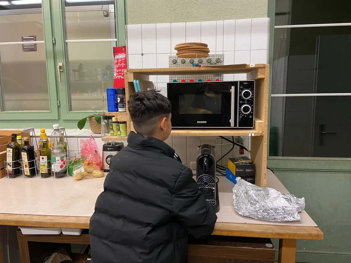 Der Zwölfjährige wärmt sich selber einen Kebab in der Mikrowelle auf. Ein Junge steht in einer Küche vor einer Mikrowelle.